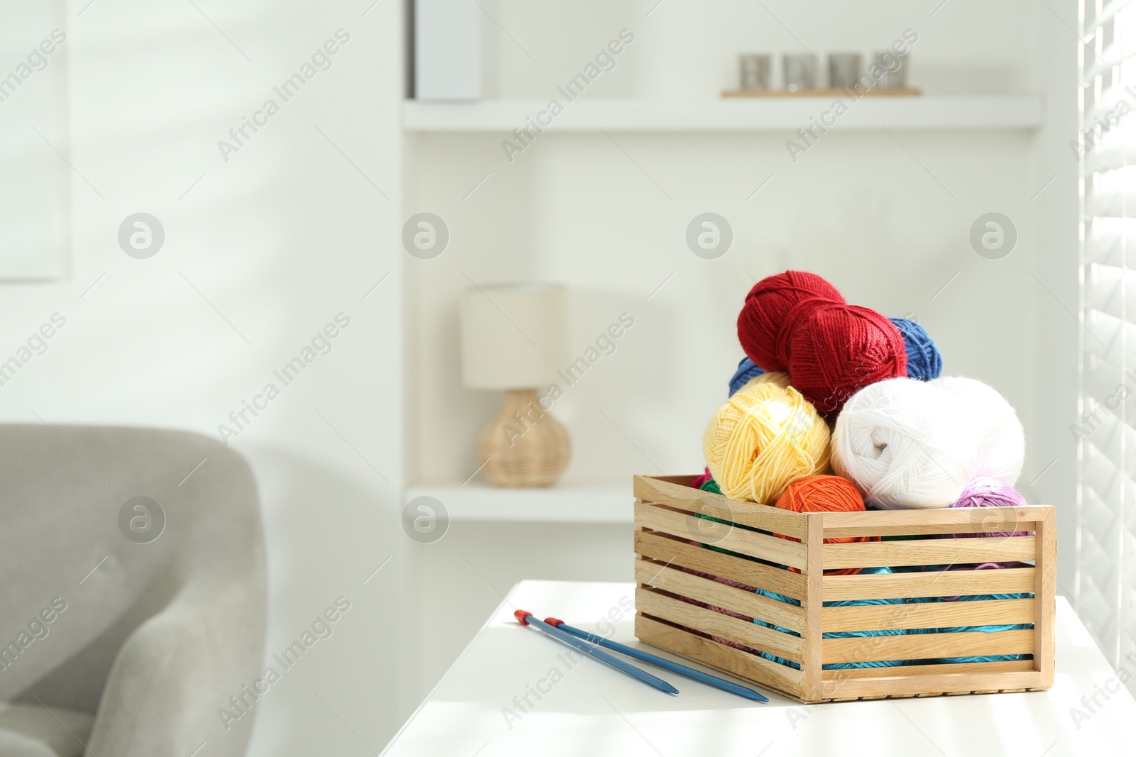 Photo of Skeins of soft yarn in crate and knitting needles on white table indoors