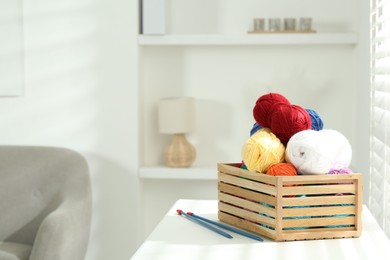 Skeins of soft yarn in crate and knitting needles on white table indoors