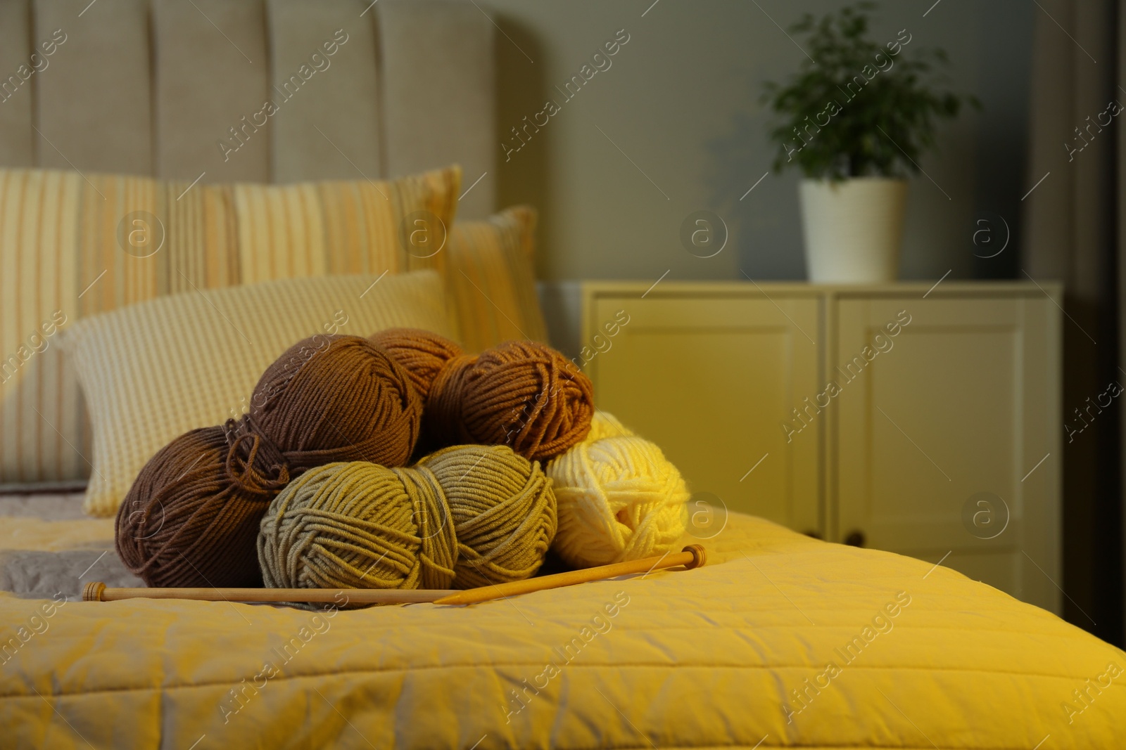 Photo of Skeins of soft yarn and knitting needles on bed indoors