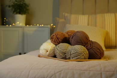 Photo of Skeins of soft yarn and knitting needles on bed indoors