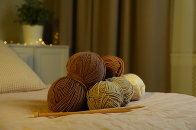 Photo of Skeins of soft yarn and knitting needles on bed indoors