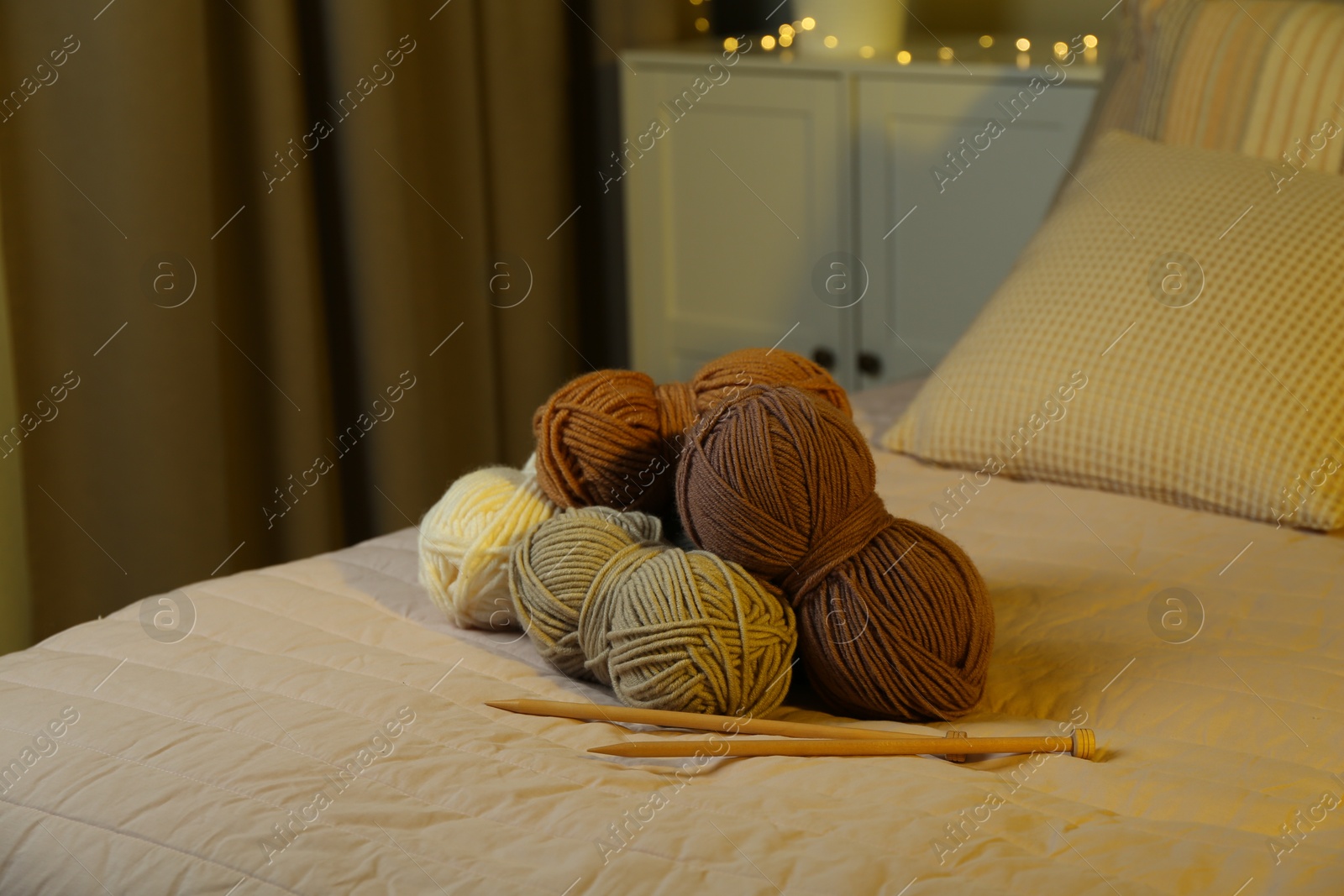 Photo of Skeins of soft yarn and knitting needles on bed indoors