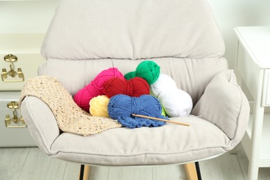 Photo of Skeins of soft yarn, crochet hook and knitting sample on armchair indoors