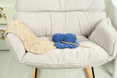 Photo of Skein of soft yarn, crochet hook and knitting sample on armchair indoors