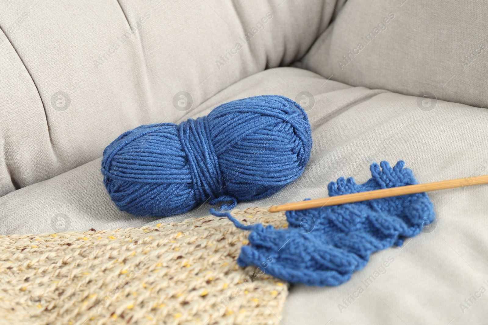 Photo of Skein of soft yarn, crochet hook and knitting sample on armchair indoors