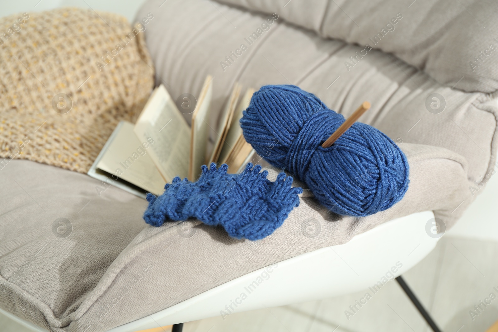 Photo of Skein of soft yarn, crochet hook and knitting sample on armchair indoors