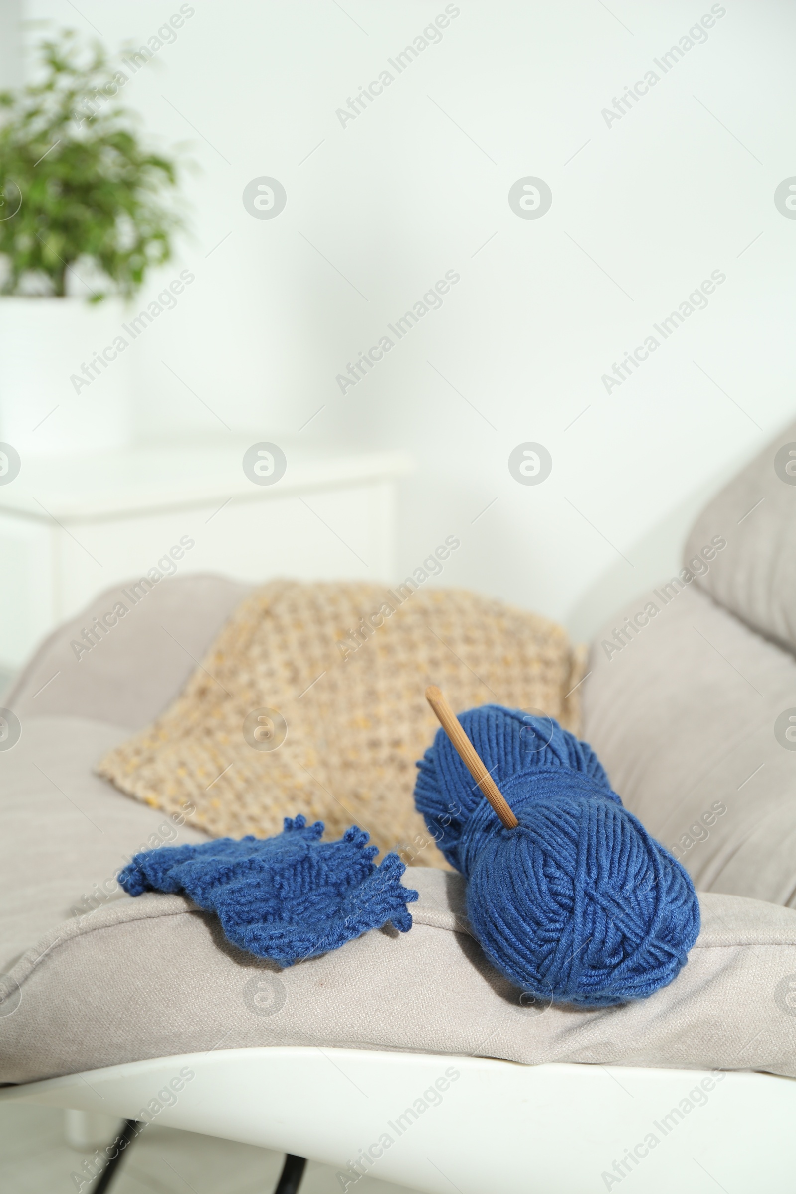 Photo of Skein of soft yarn, crochet hook and knitting sample on armchair indoors