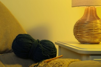 Photo of Skein of soft yarn, crochet hook and knitting sample on sofa indoors