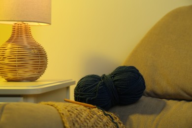 Photo of Skein of soft yarn, crochet hook and knitting sample on sofa indoors