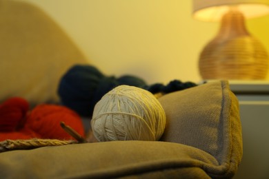 Photo of Knitting material. Skeins of soft yarn and crochet hook on sofa indoors