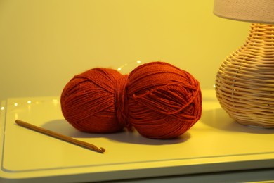 Photo of Knitting material. Skein of soft yarn, crochet hook and lamp on table indoors