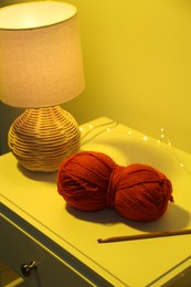 Knitting material. Skein of soft yarn, crochet hook and lamp on bedside table indoors