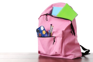 Backpack with different school stationery on wooden table against white background, space for text