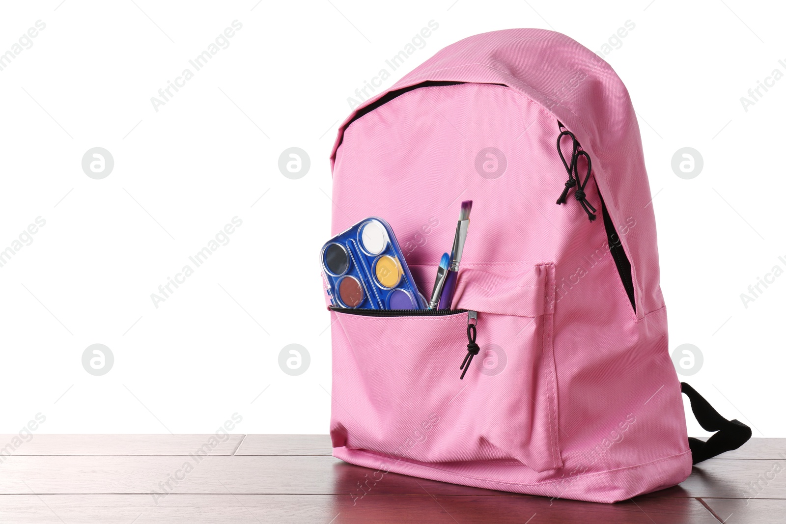 Photo of Backpack with watercolor palette and brushes on wooden table against white background, space for text