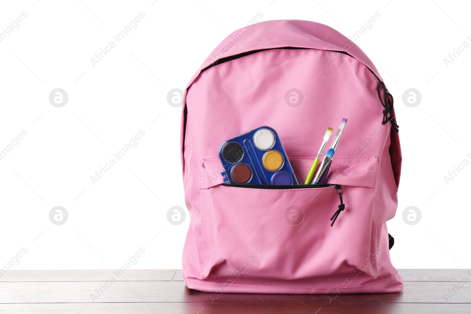 Photo of Backpack with watercolor palette and brushes on wooden table against white background, space for text