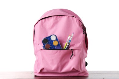 Photo of Backpack with watercolor palette and brushes on wooden table against white background