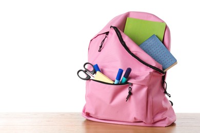 Photo of Backpack with different school stationery on wooden table against white background, space for text