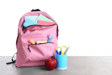 Photo of Backpack with different school stationery and apple on gray textured table against white background, space for text