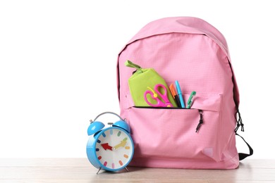 Photo of Backpack with different school stationery and alarm clock on wooden table against white background, space for text