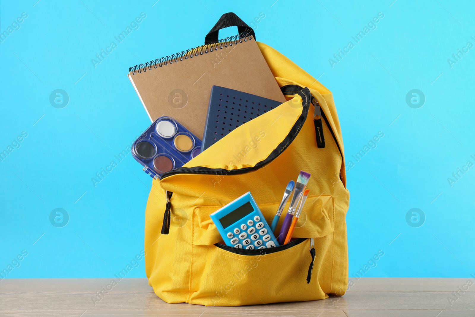 Photo of Backpack with different school stationery on wooden table against light blue background