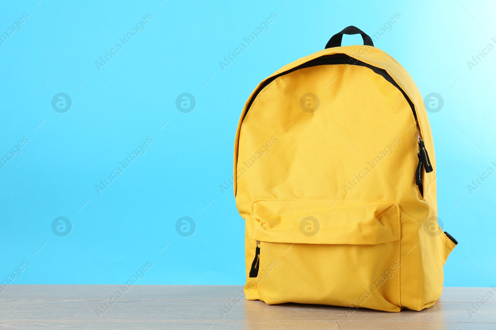 Photo of Yellow backpack on wooden table against light blue background, space for text