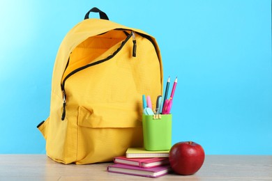 Photo of Backpack with different school stationery and apple on wooden table against light blue background, space for text