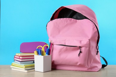 Backpack with different school stationery on wooden table against light blue background