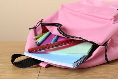 Photo of Backpack with different school stationery on wooden table against beige background, closeup