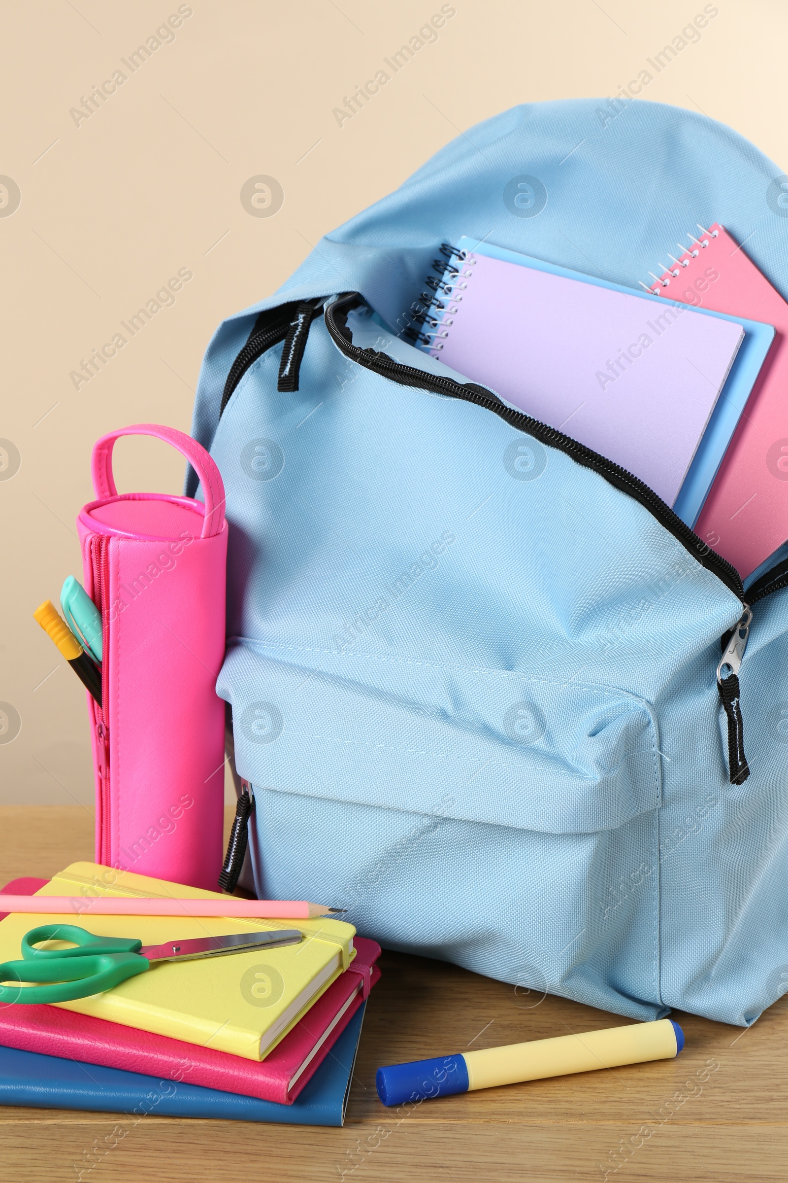 Photo of Backpack with different school stationery on wooden table against beige background