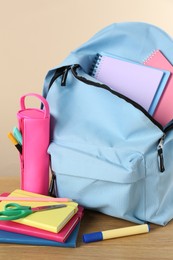 Backpack with different school stationery on wooden table against beige background