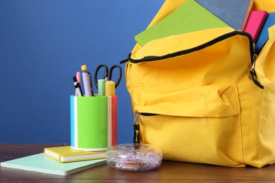 Photo of Backpack with different school stationery on wooden table against blue background