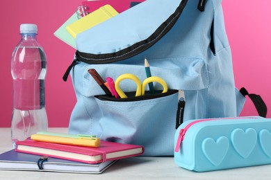 Photo of Backpack with different school stationery and bottle of water on light table against pink background, closeup