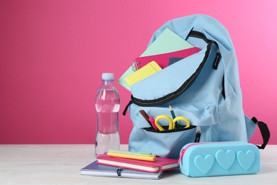 Photo of Backpack with different school stationery and bottle of water on light table against pink background, space for text