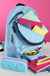 Backpack with different school stationery on light table against pink background