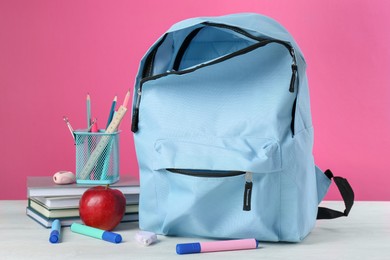 Photo of Backpack with different school stationery and apple on light table against pink background