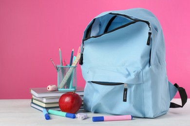 Photo of Backpack with different school stationery and apple on light table against pink background