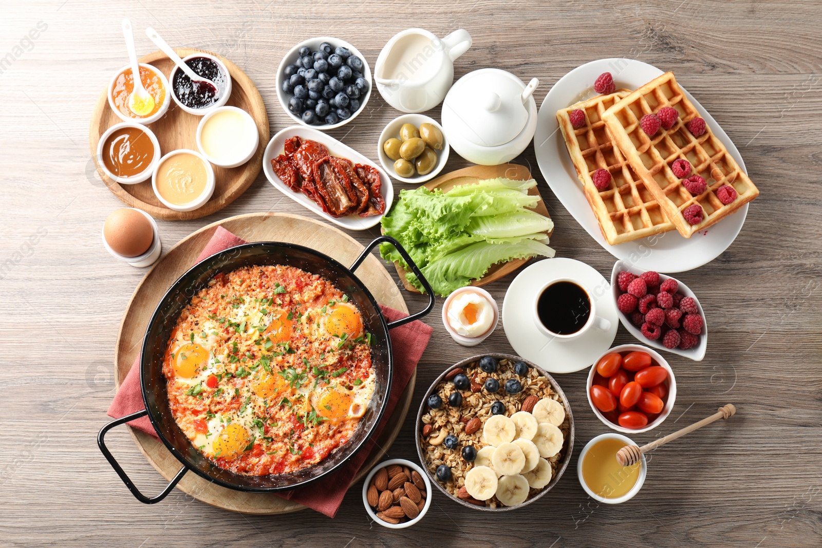 Photo of Tasty shakshouka in frying pan and other meals served for breakfast on wooden table, flat lay