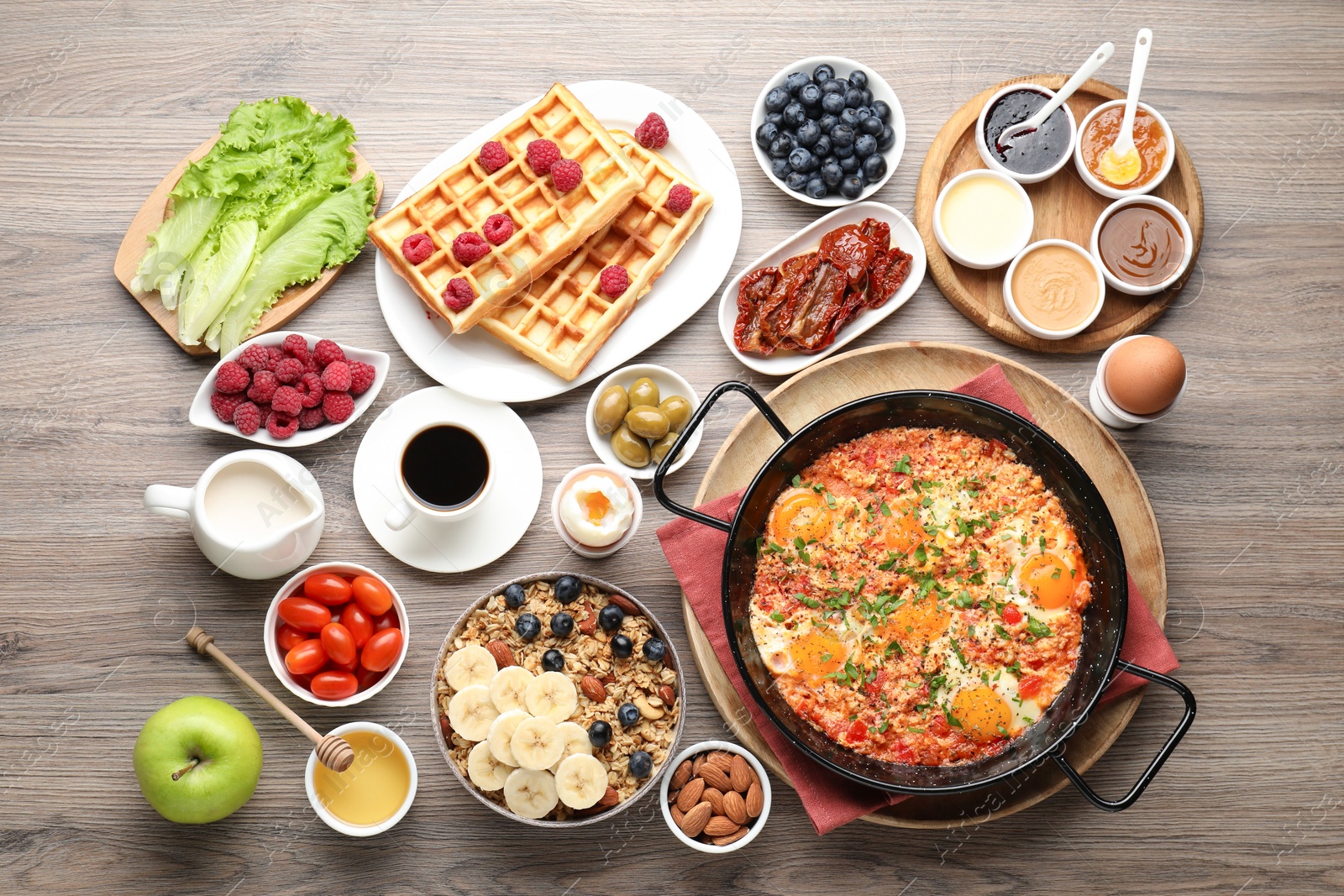 Photo of Tasty shakshouka in frying pan and other meals served for breakfast on wooden table, flat lay