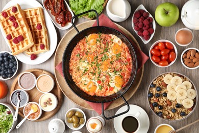 Photo of Tasty shakshouka in frying pan and other meals served for breakfast on wooden table, flat lay