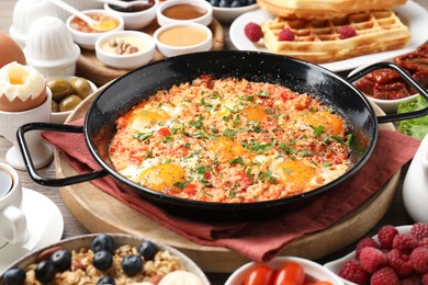 Tasty shakshouka in frying pan and other meals served for breakfast on wooden table