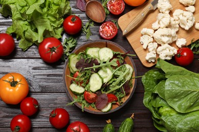 Photo of Healthy vegetarian food. Salad in bowl and vegetables on wooden table, flat lay