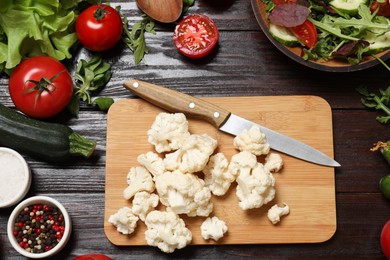 Photo of Healthy vegetarian food. Pieces of cauliflower, salad, peppercorns and vegetables on wooden table, flat lay