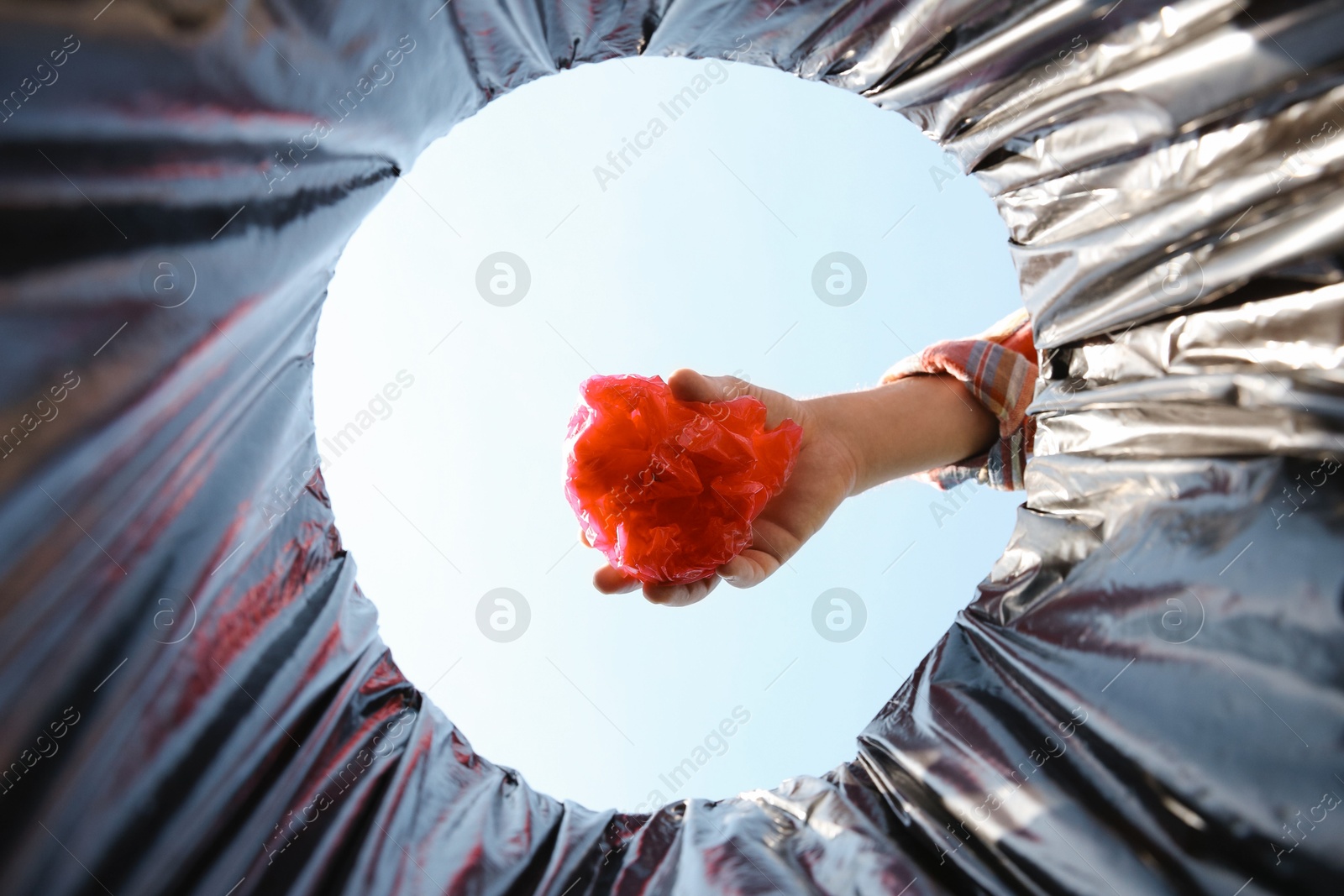 Photo of Man throwing garbage into trash bin outdoors, bottom view