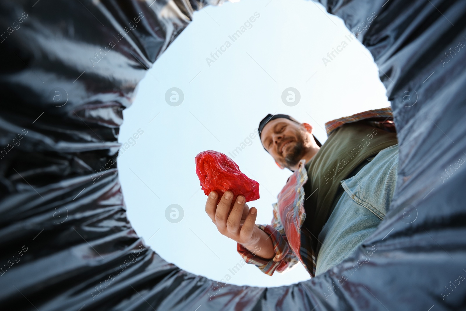 Photo of Man throwing garbage into trash bin outdoors, bottom view