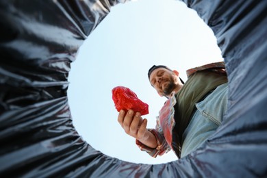 Photo of Man throwing garbage into trash bin outdoors, bottom view