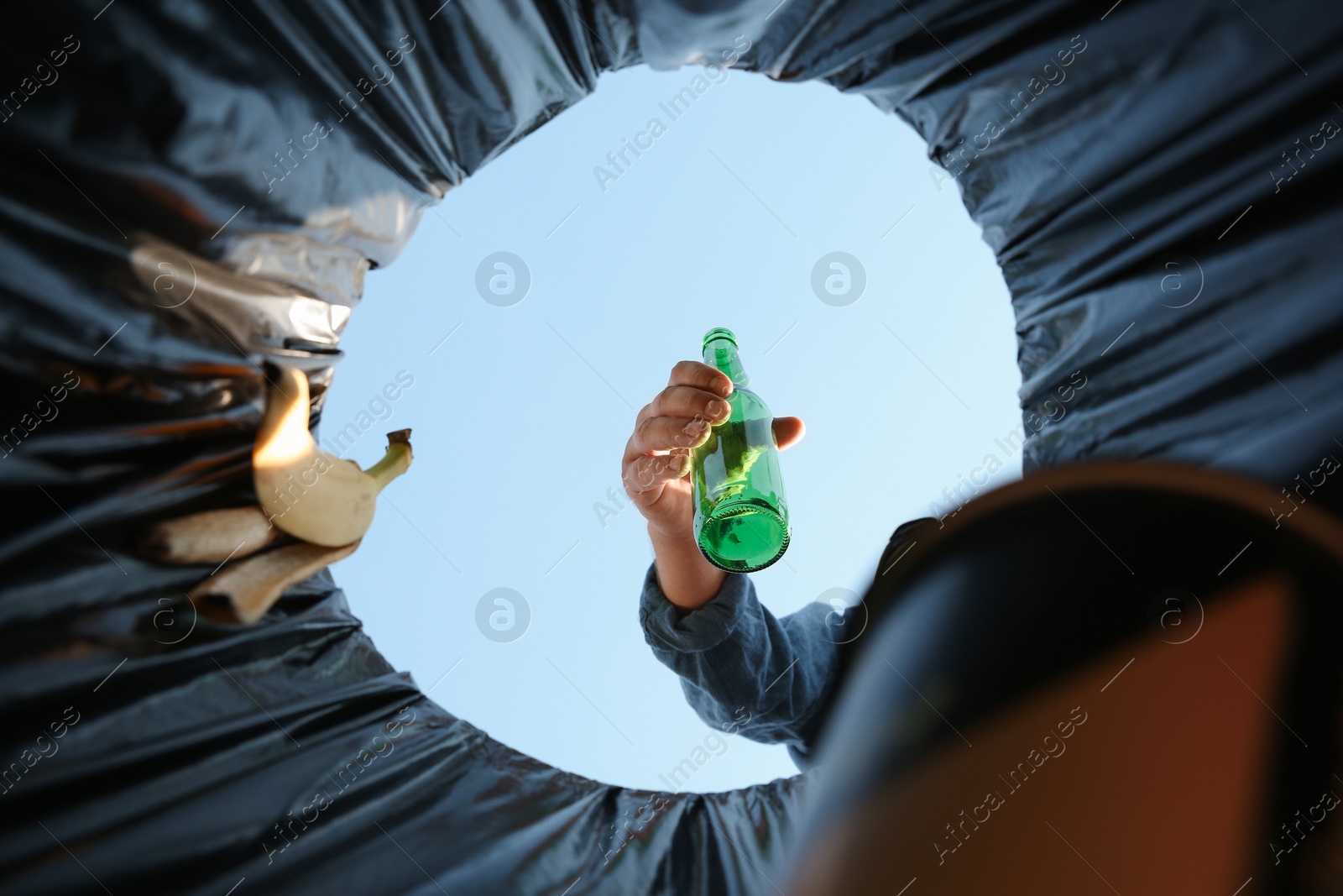 Photo of Man throwing glass bottle into garbage bin outdoors, bottom view