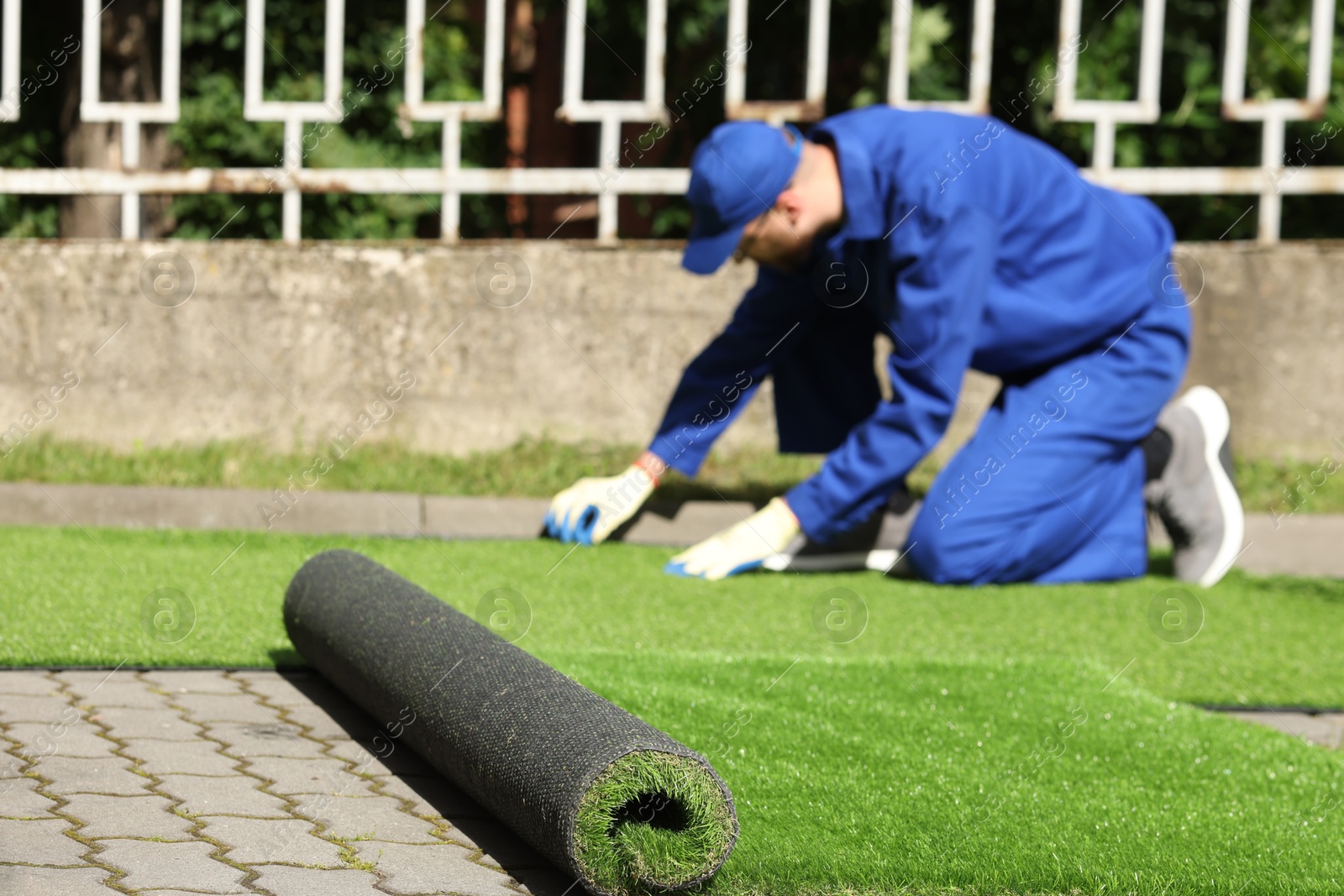 Photo of Young man in uniform installing artificial turf outdoors, selective focus