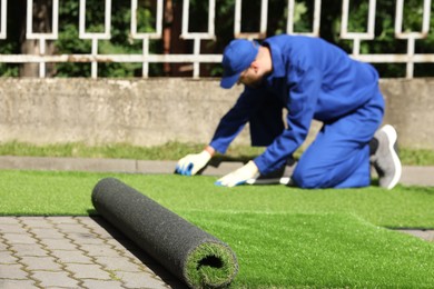 Photo of Young man in uniform installing artificial turf outdoors, selective focus