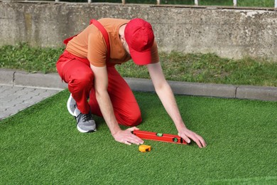 Young man in uniform installing artificial turf outdoors