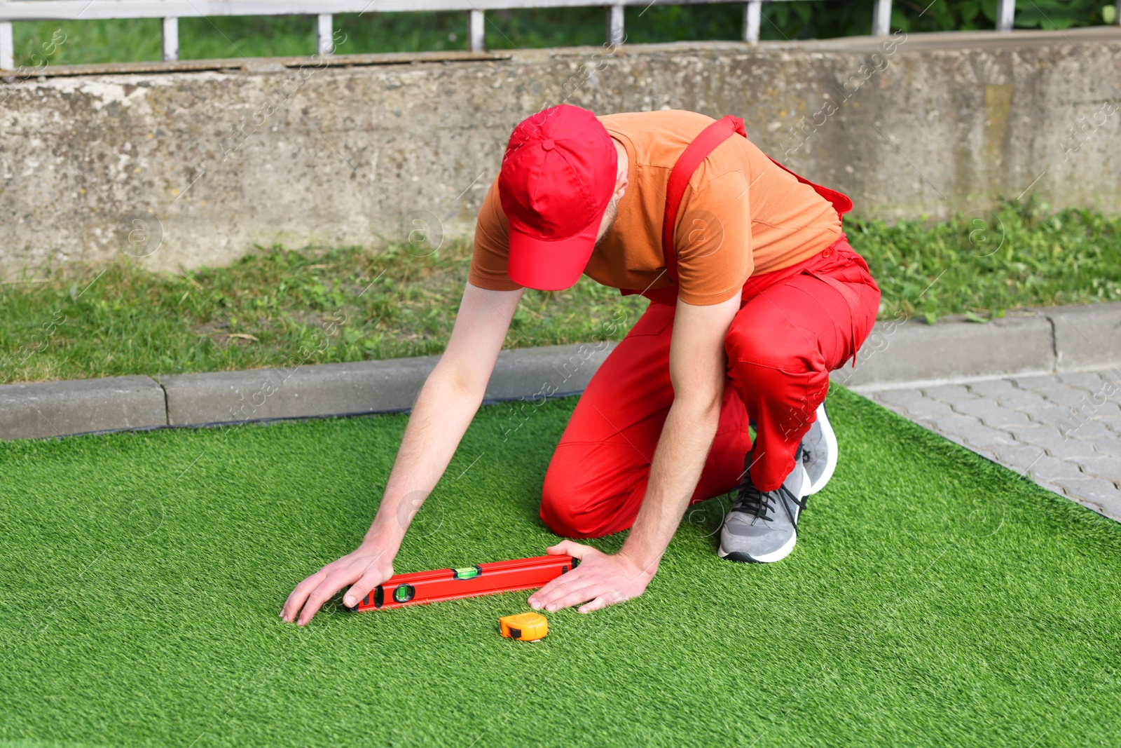 Photo of Young man in uniform installing artificial turf outdoors